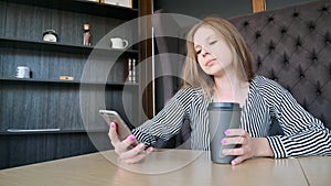 Smartphone girl using app on phone drinking coffee smiling in cafe. Beautiful young casual female professional on mobile