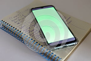 A smartphone with a green screen lies on a schoolchild's notepad