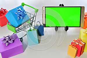 Smartphone with green screen, a miniature shopping cart with a box and colorful shopping bags