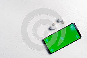 Smartphone with gren screen mockup and white wireless headphones isolated on white background