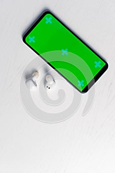 Smartphone with gren screen mockup and white wireless headphones isolated on white background