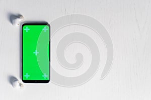 Smartphone with gren screen mockup and white wireless headphones isolated on white background