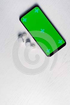 Smartphone with gren screen mockup and white wireless headphones isolated on white background