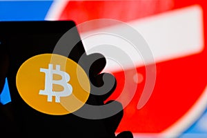 Smartphone in hand with Bitcoin cryptocurrency logo. Prohibiting red sign on background.