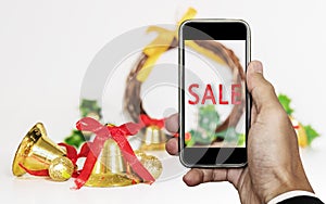 Smartphone on hand with `SALE` on screen, with Christmas decorations ornament, Holiday Christmas Sale