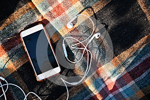 Smartphone with headphones on the cozy sweaters. Top view. Autumn flatlay. Outdoor listening podcasts