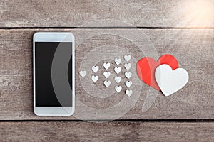 Smartphone and hearts paper on wooden background photo