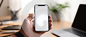 The smartphone held in hand showcasing a blank screen in a modern workspace. AI generated image