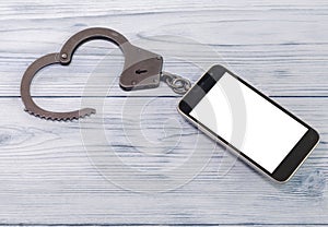 Smartphone, iron handcuffs on a wooden background.