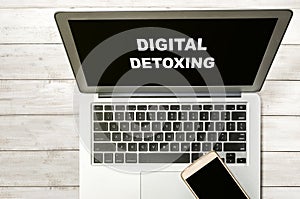 Smartphone and laptop with Digital Detoxing text on wooden table