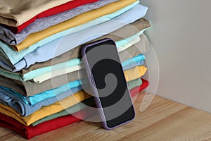Smartphone leaning on stack of folded clothes on wooden table