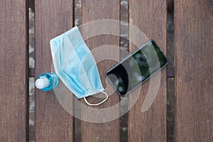 Smartphone, Mask and alcohol spray placed on a wooden balcony