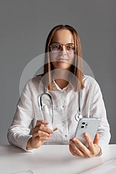 Smartphone for medical work. Pleased woman doctor wearing white medical lab coat stethoscope and glasses holding cell phone and