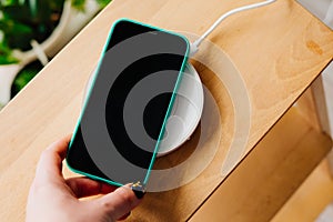 Smartphone in mint silicone case is charged from a wireless charger.