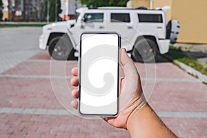 Smartphone mockup in the hand of a man. Against the background of a white SUV. Online purchase, car rental. The concept of road