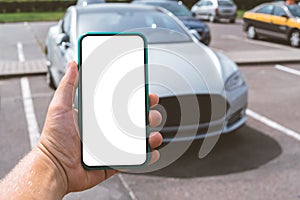 Smartphone mockup in the hands of a man. Against the background of a white electric car.