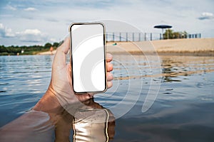 Smartphone mockup with reflections in the water in a man`s hand. Against the backdrop of the beach with blue skies. Time for rest