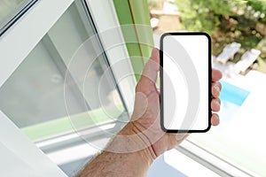 Smartphone mockup screen, man holding mobile phone with blank touchscreen next to the apartment window with view of the outdoor