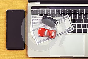 Smartphone near Car model, money and Notebook on wooden desk. shopping online and car payment by using laptop