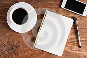 Smartphone with notebook and cup of coffee on wooden background.