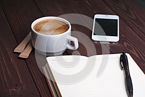 Smartphone with notebook and cup of strong coffee on wooden background