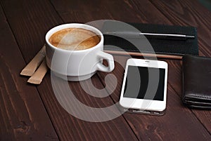 Smartphone with notebook and cup of strong coffee on wooden background