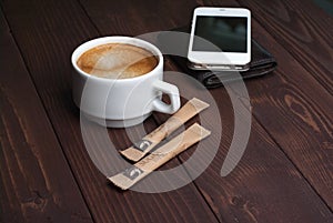 Smartphone with notebook and cup of strong coffee on wooden background