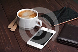 Smartphone with notebook and cup of strong coffee on wooden background