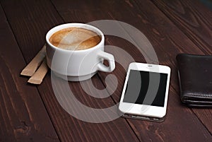 Smartphone with notebook and cup of strong coffee on wooden background