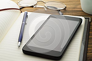 Smartphone and notebook on wood table.