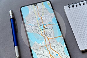 Smartphone, notepad and pencil on gray. Map city of Seattle on screen device. Seattle is city on shores of Puget Sound, largest