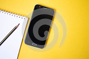 Smartphone, notepad and pencil on yellow background