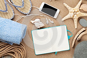 Smartphone and notepad on sea sand with starfish and shells