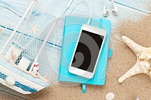 Smartphone and notepad on sea sand with starfish and toy boat