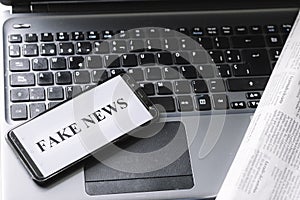 Smartphone with the phrase fake news written on the screen on a laptop, newspaper and magnifying glass photo