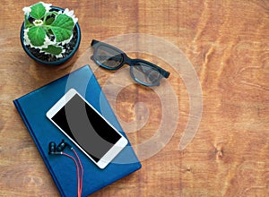 Smartphone with red earphones, blue notebook and black eyeglasses on wooden background. View from above