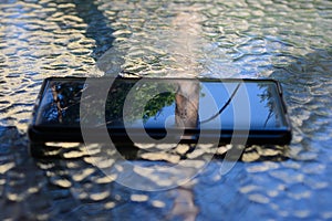 Smartphone with a reflection of the sky and trees in the screen, lying on a glass table