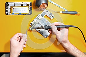 Smartphone repair in a service center. Hands of a professional master repairman repairing disassembled into pieces cell phone.