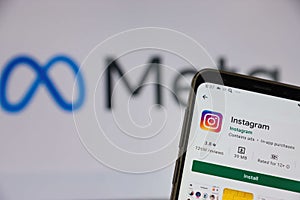 The smartphone screen on which the Instagram application is installed against the background of the Meta Facebook logo. There is a