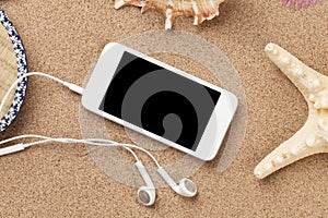 Smartphone on sea sand with starfish and shells