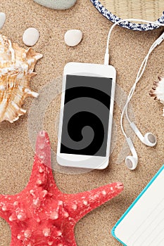 Smartphone on sea sand with starfish and shells