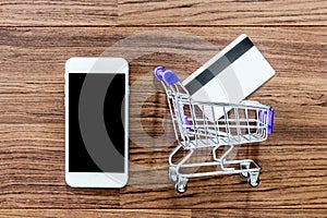 Smartphone with shopping basket and credit card on wooden background - Online shopping concept