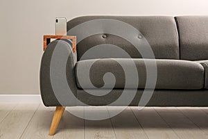 Smartphone on sofa with wooden armrest table in room. Interior element