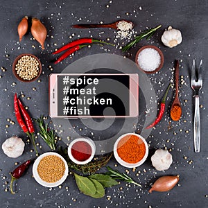 Smartphone, spices, vegetables and fork for meat on a dark background. Hashtags spie smartphone meat, chicken and fish on th