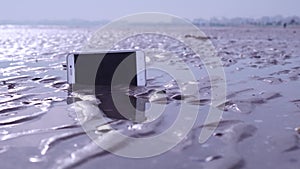 Smartphone stuck in the wet sand of the beach