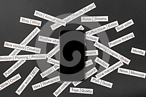 Smartphone surrounded by a cloud of words on business themes cut out of paper on a gray background