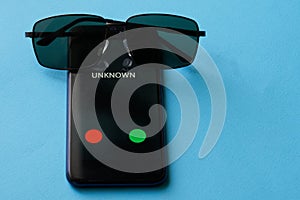 A smartphone with an undetermined ring is lying on a blue surface along with sunglasses. The problem of secrecy, anonymity and