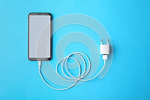 Smartphone and USB charger on blue background, flat lay. Modern technology