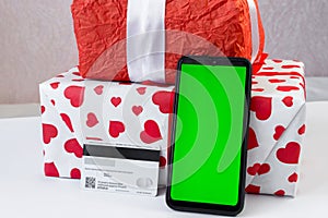 Smartphone with vertical green screen, bank card and Christmas gifts on the table. Online shopping festive internet concept.