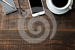 Smartphone white and a cup with coffee glasses and a notepad on a brown wooden table. view from above